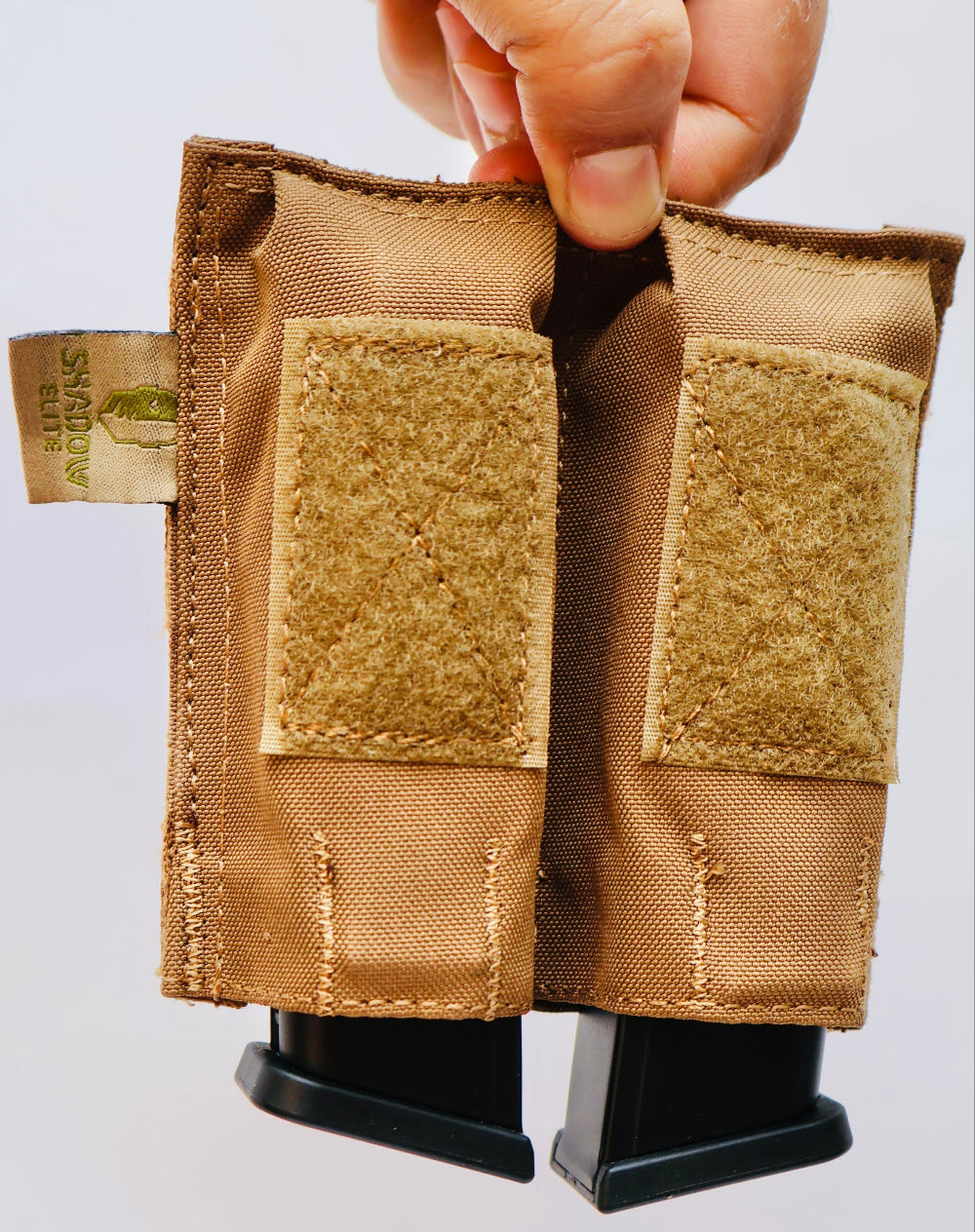 Tan tactical magazine pouch with Velcro patches held by a hand on a light gray background