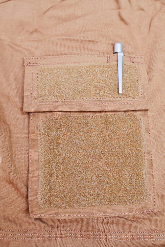 Close-up of a tan fabric Aram pocket of Combat shirt with two patches and a pen on a matching background